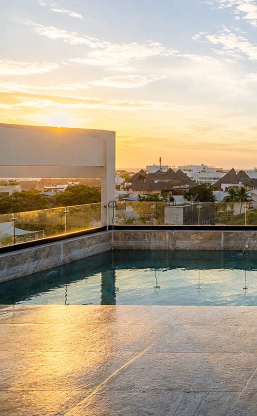 El sol poniéndose sobre la alberca del rooftop de Marbella, con Playa del Carmen detrás